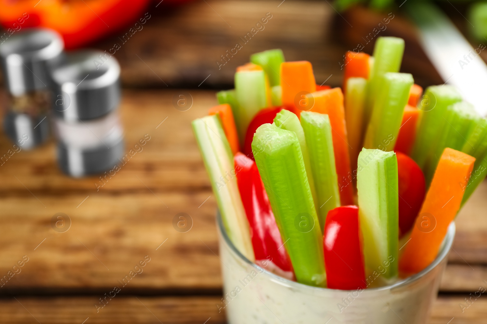 Photo of Celery and other vegetable sticks with dip sauce in glass bowl on wooden table, closeup. Space for text