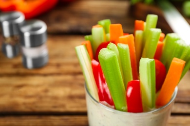 Celery and other vegetable sticks with dip sauce in glass bowl on wooden table, closeup. Space for text