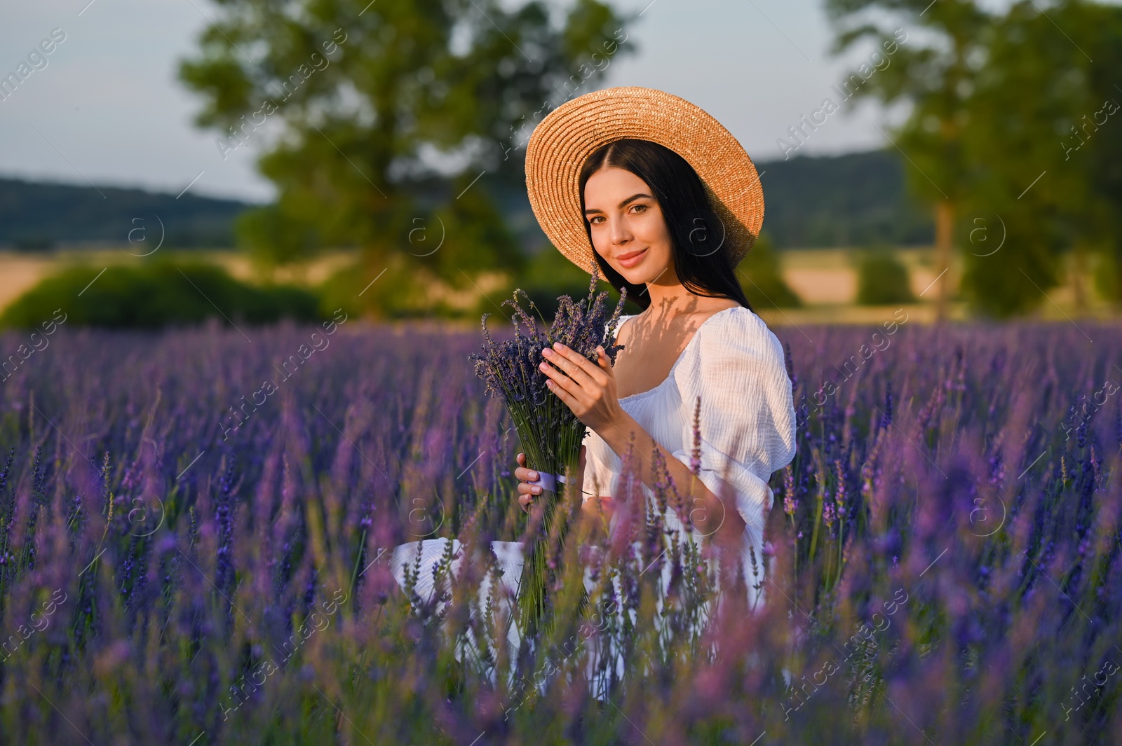 Photo of Beautiful young woman with bouquet sitting in lavender field