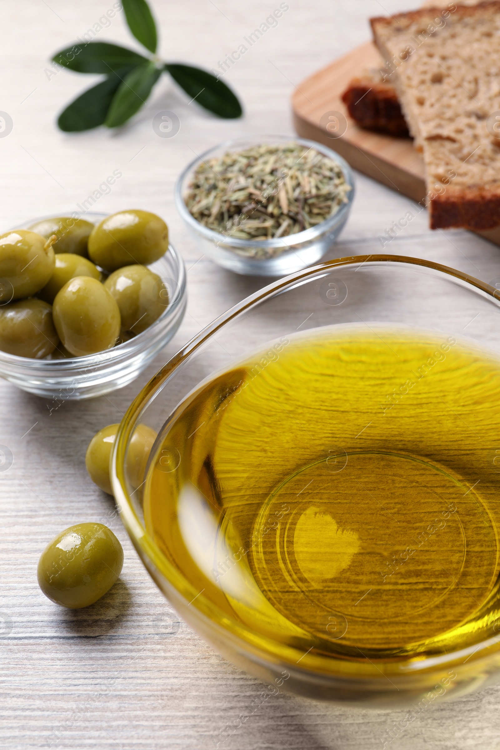 Photo of Glass bowl with fresh olive oil on white wooden table, closeup