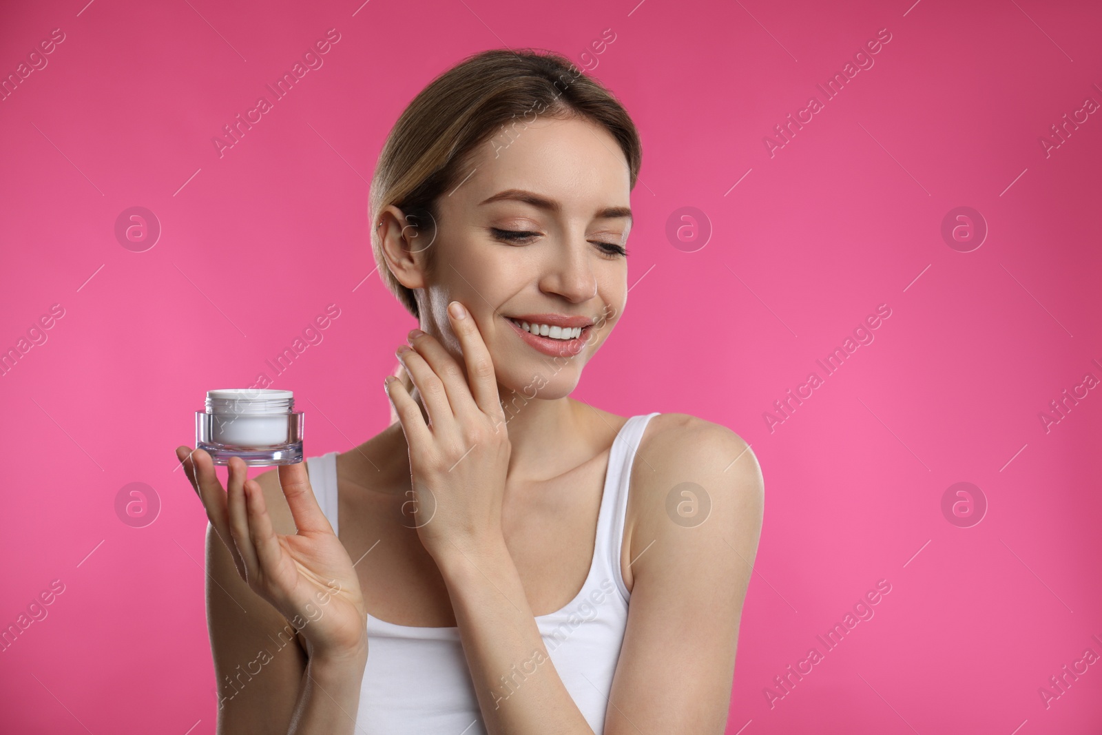 Photo of Young woman applying facial cream on pink background