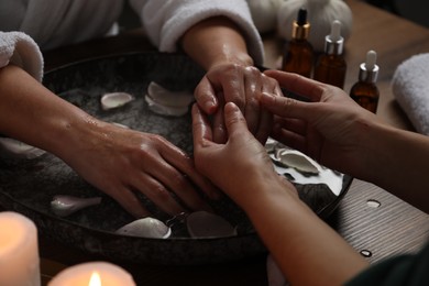 Photo of Woman receiving hand massage in spa salon, closeup. Bowl of water and flower petals on table