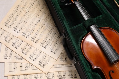Violin in case and music sheets on table, top view