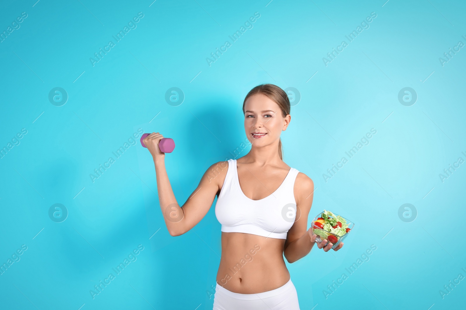 Photo of Slim woman with salad and dumbbell on color background. Healthy diet