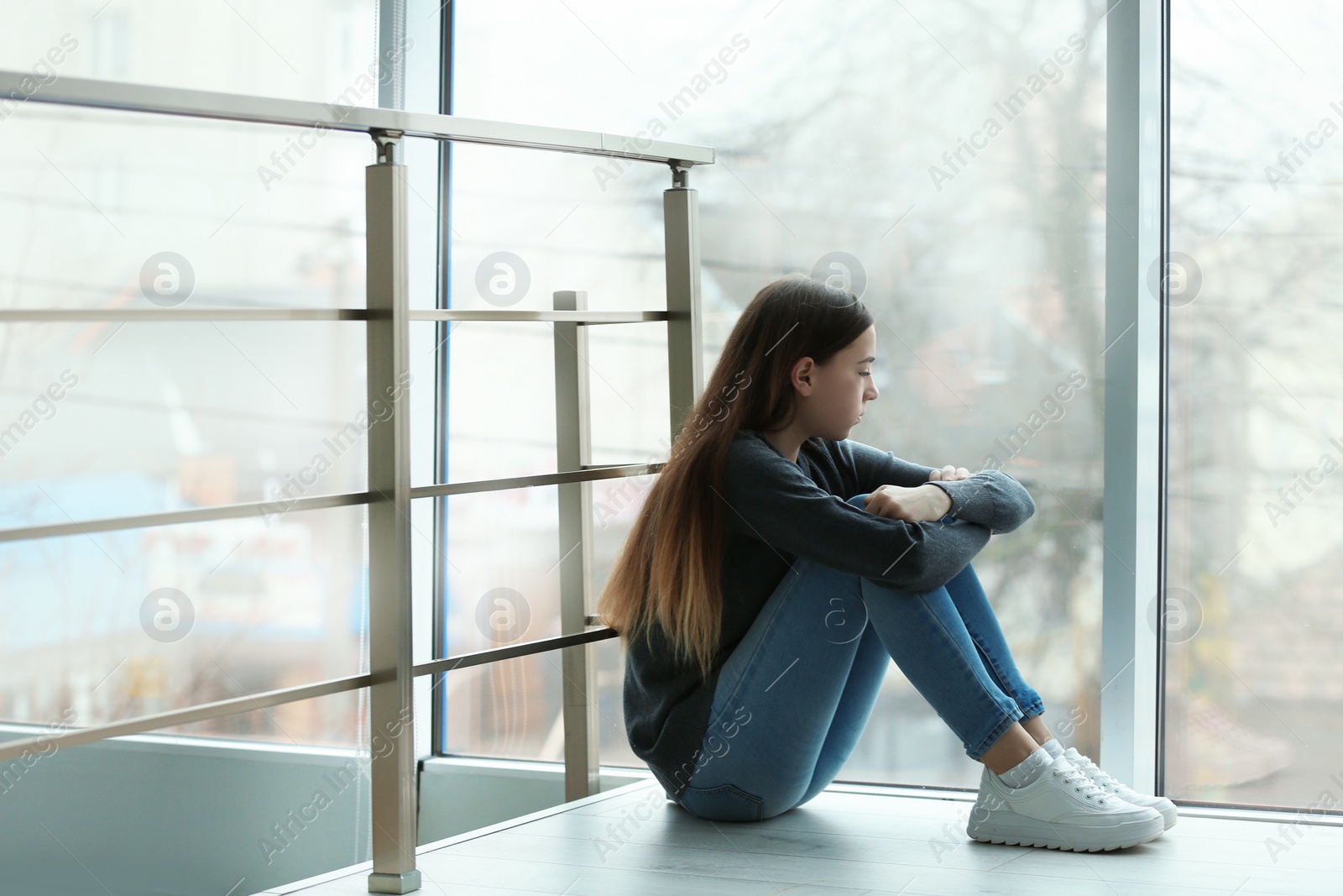 Photo of Upset teenage girl sitting at window indoors. Space for text