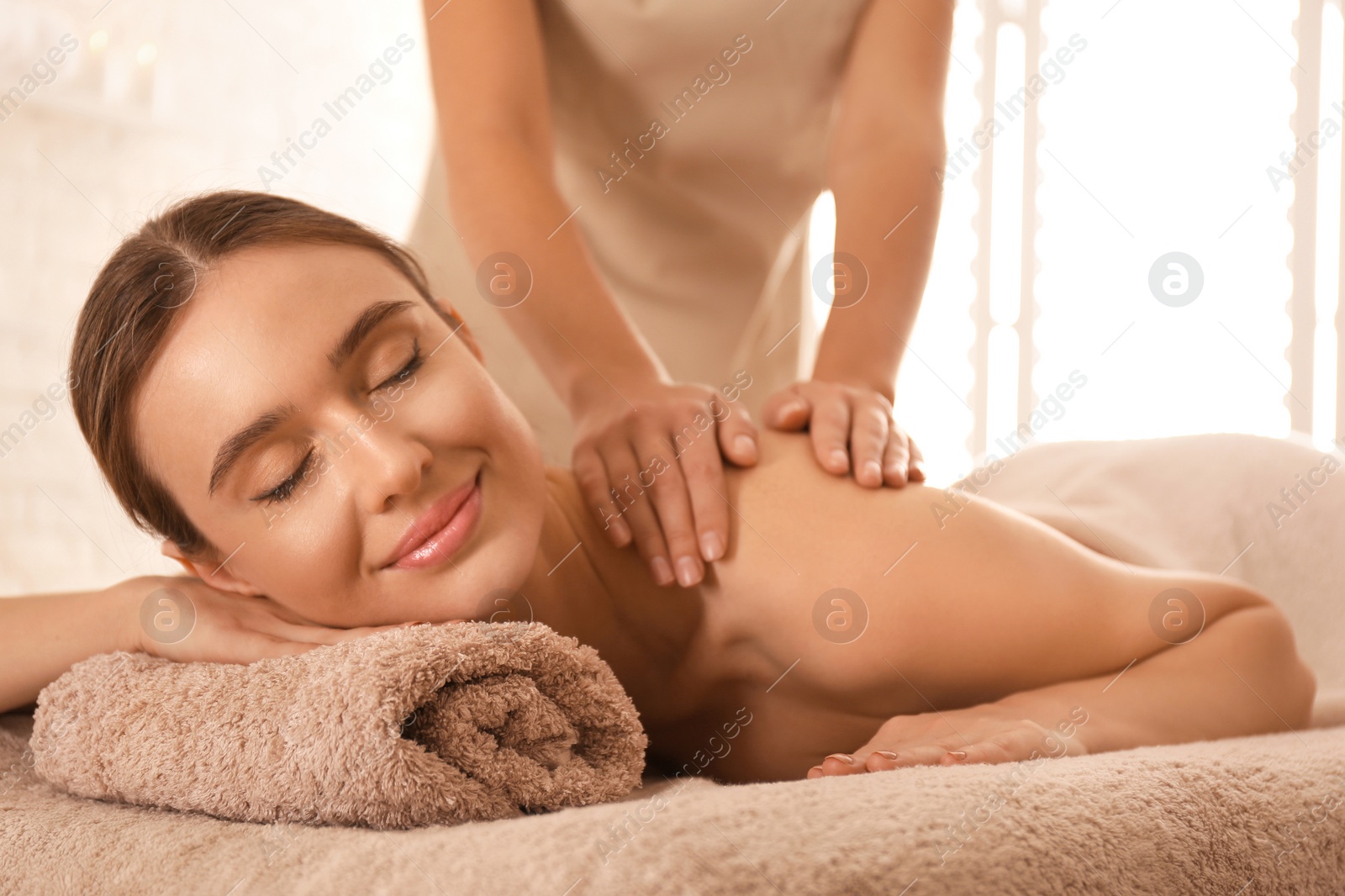 Photo of Young woman having body scrubbing procedure with sea salt in spa salon