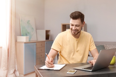 Photo of Young man working with laptop at desk in home office