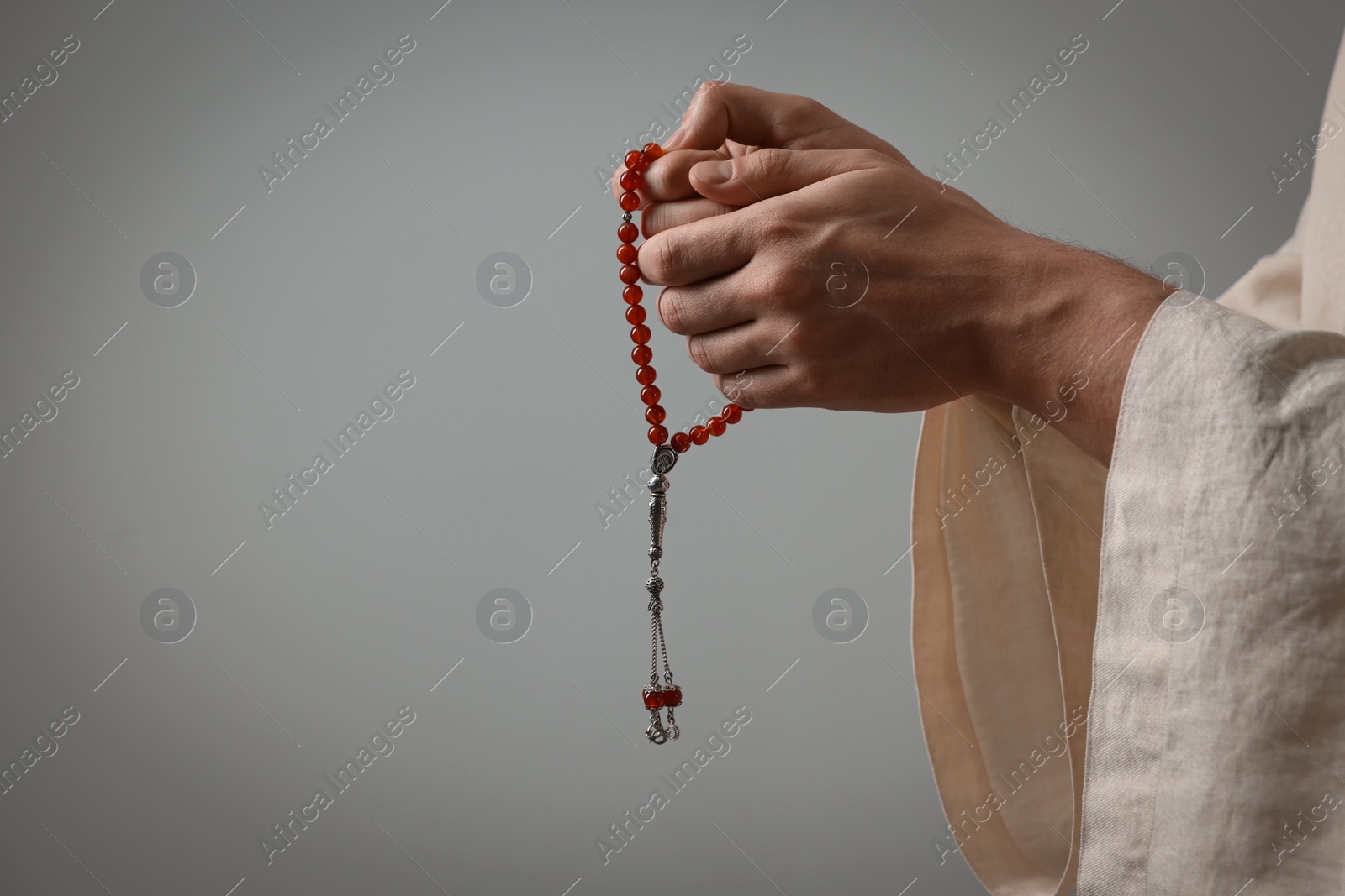 Photo of Muslim man with misbaha praying on light grey background, closeup. Space for text