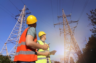 Professional electricians in uniforms near high voltage towers