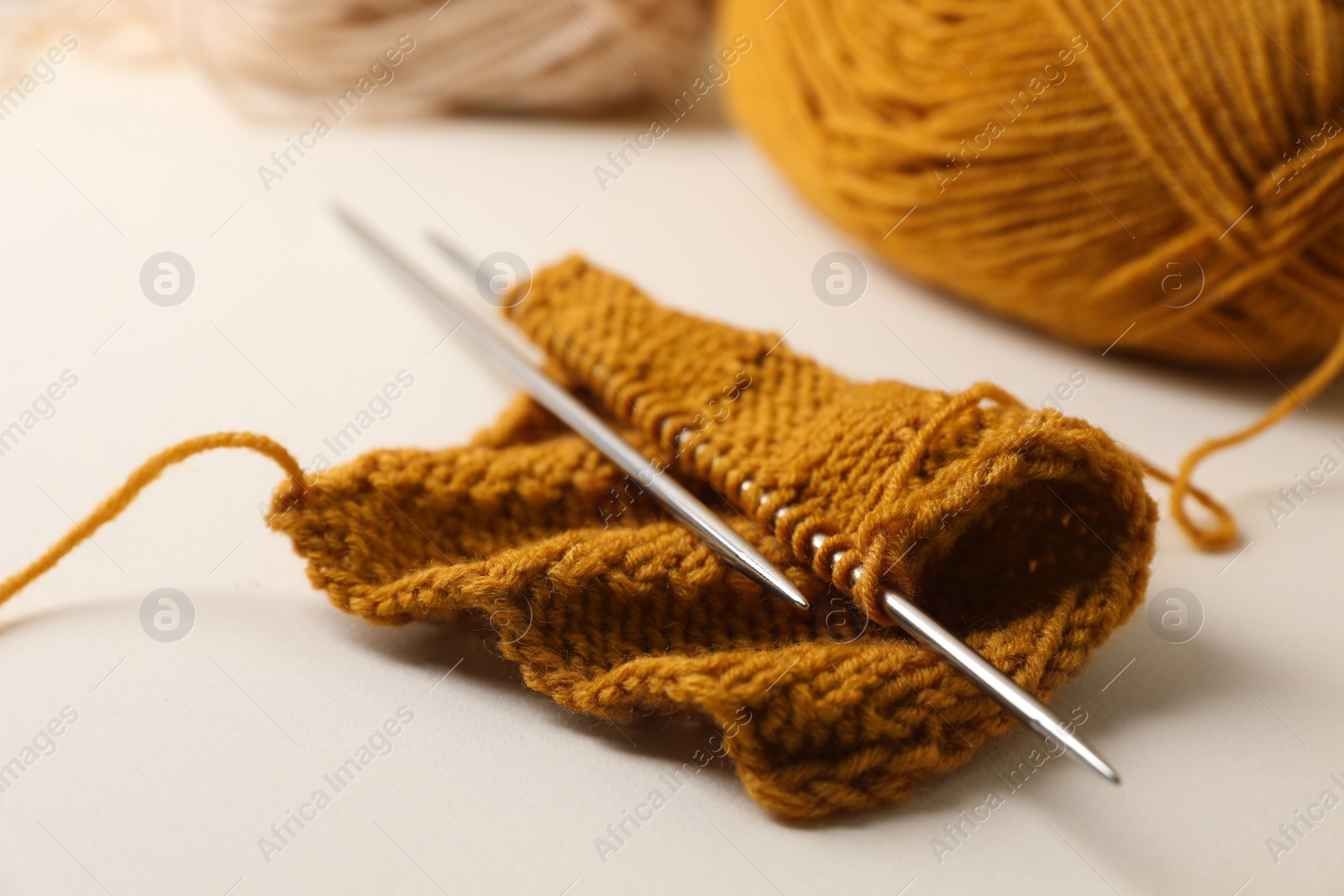 Photo of Soft orange knitting and metal needles on beige background, closeup