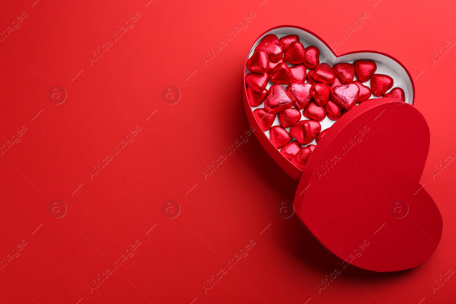 Photo of Box with heart shaped chocolate candies on red background, flat lay. Space for text