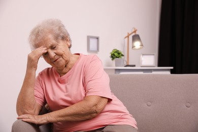 Senior woman with headache sitting on sofa at home. Space for text