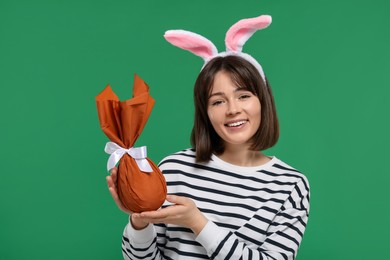 Photo of Easter celebration. Happy woman with bunny ears and wrapped egg on green background