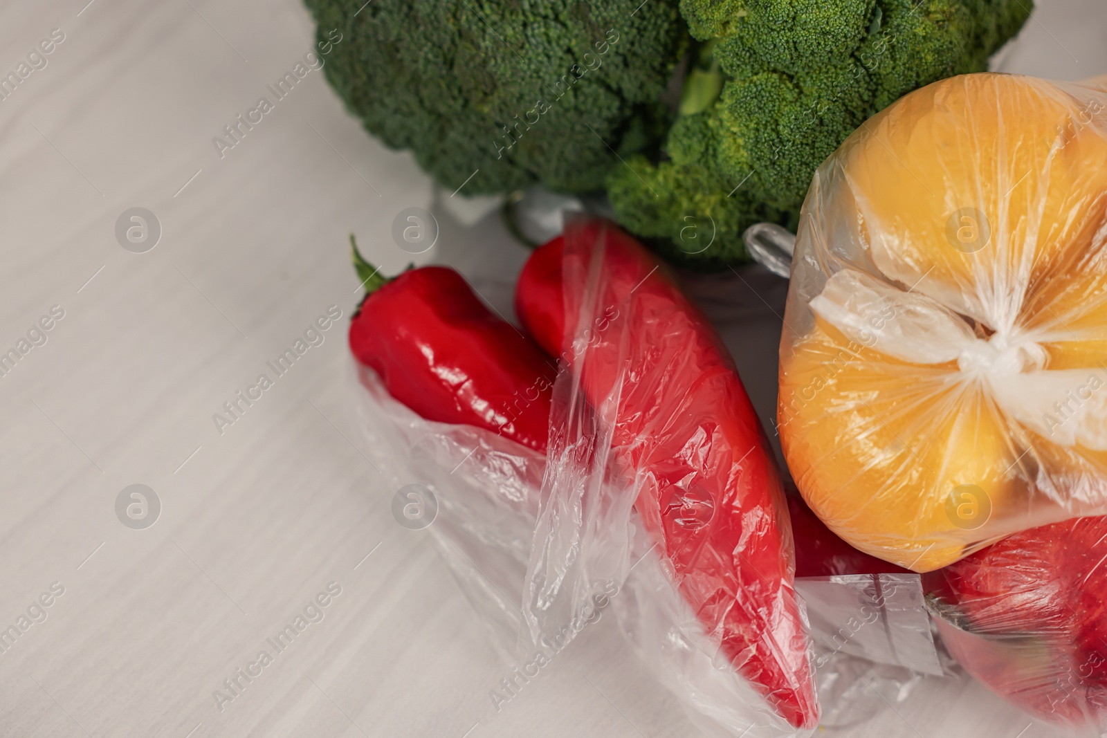 Photo of Plastic bags and fresh products on white table, above view. Space for text