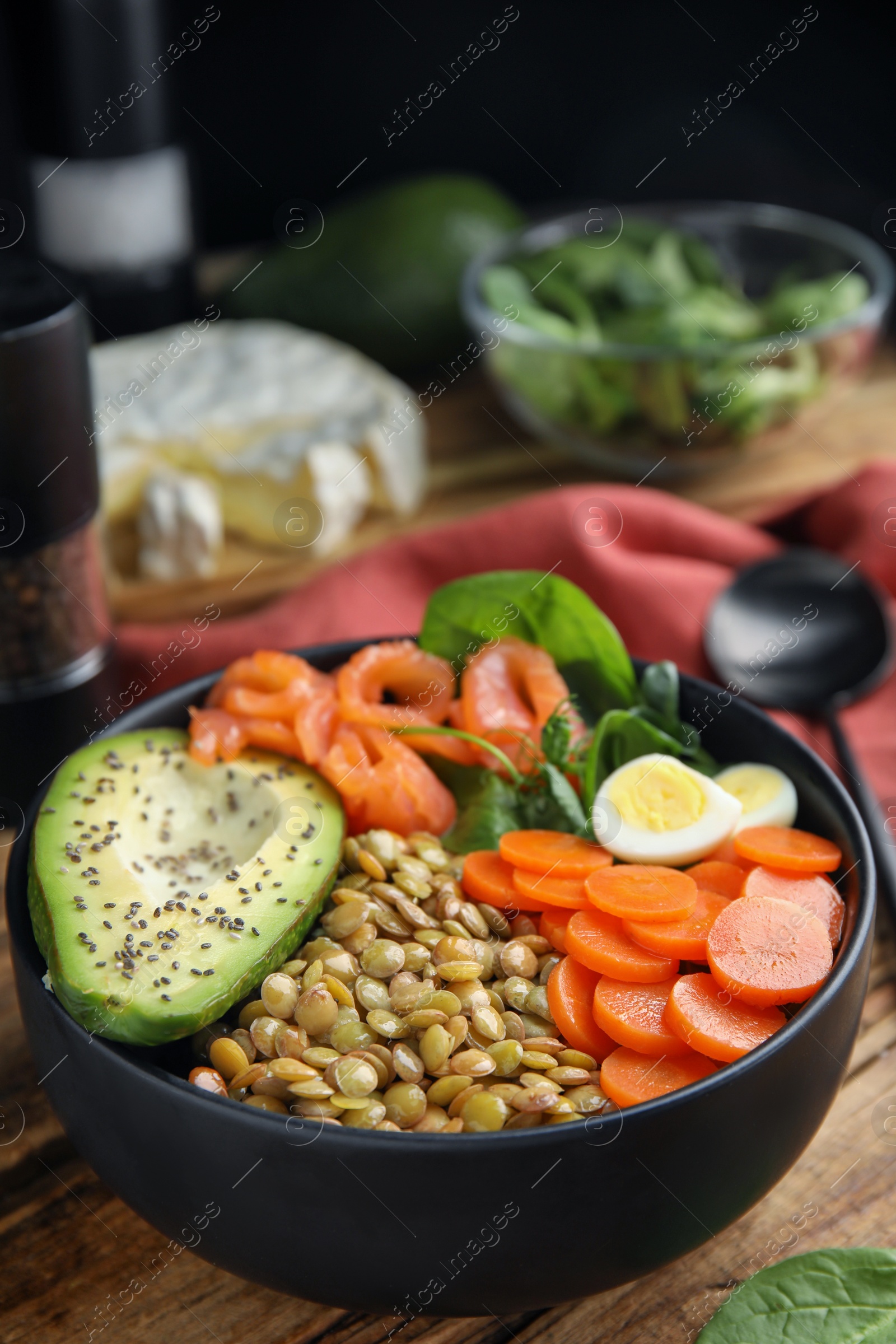 Photo of Delicious lentil bowl with carrot, avocado, egg and salmon on wooden table