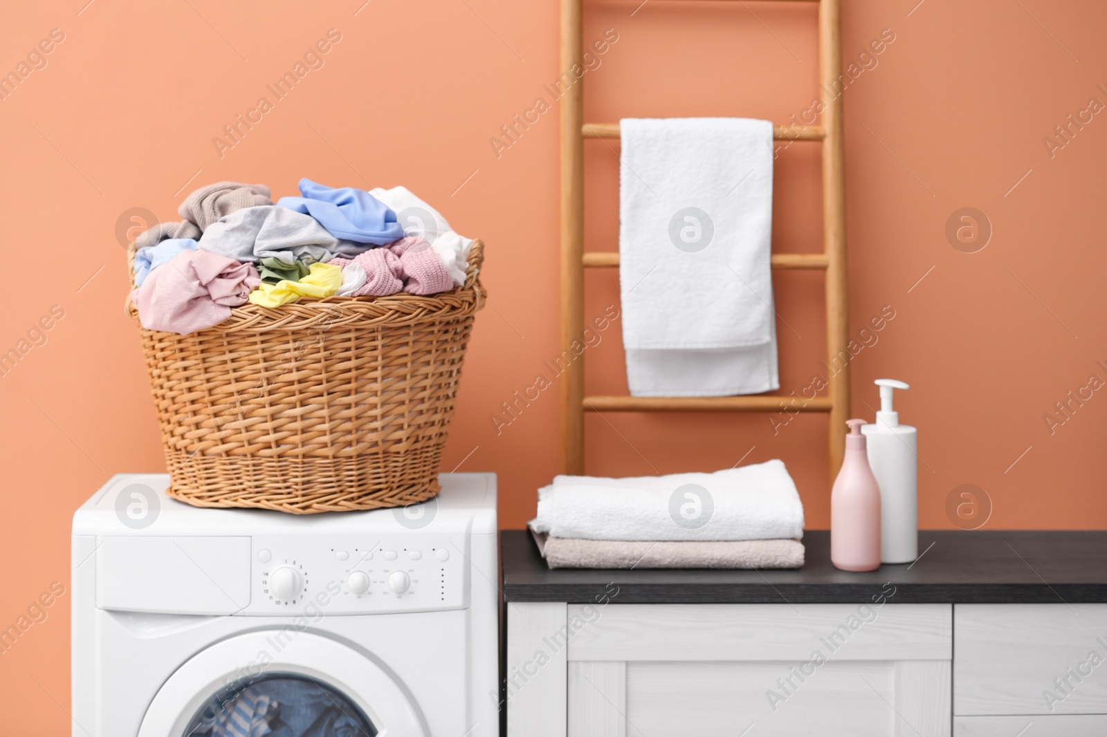 Photo of Wicker basket with dirty laundry on washing machine near coral wall indoors