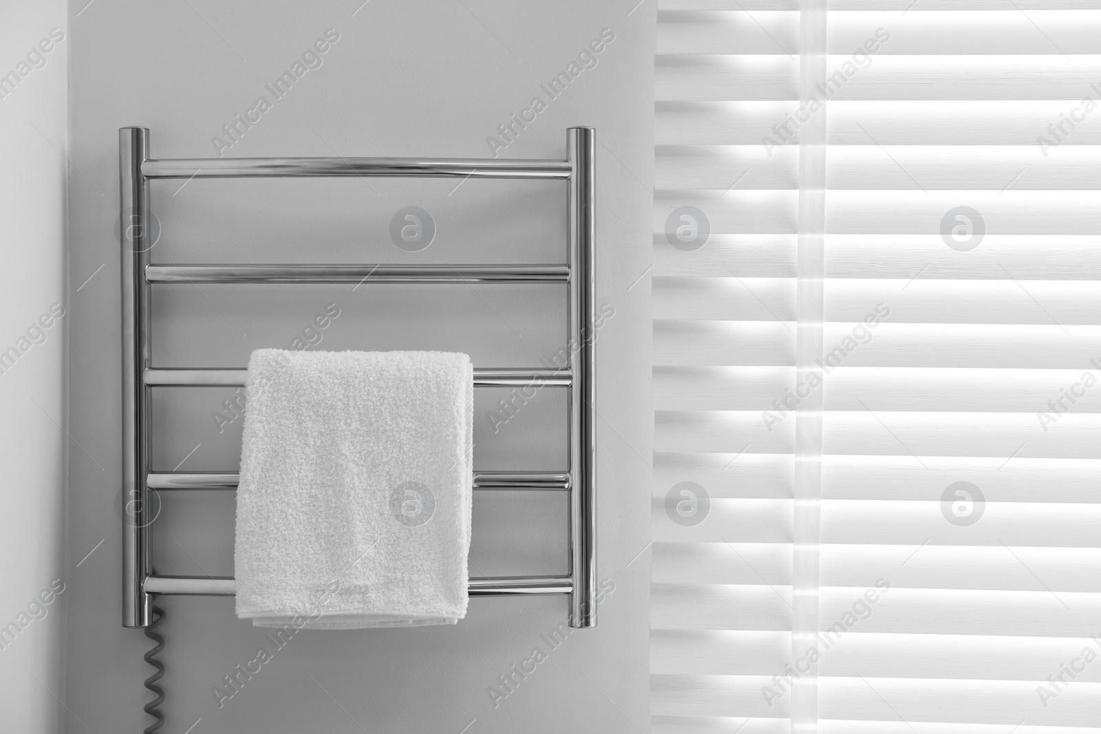 Photo of Heated rail with towel on white wall in bathroom, space for text