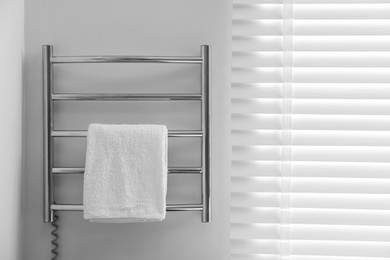 Photo of Heated rail with towel on white wall in bathroom, space for text
