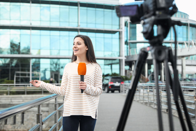 Photo of Young female journalist with microphone working on city street