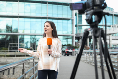 Young female journalist with microphone working on city street