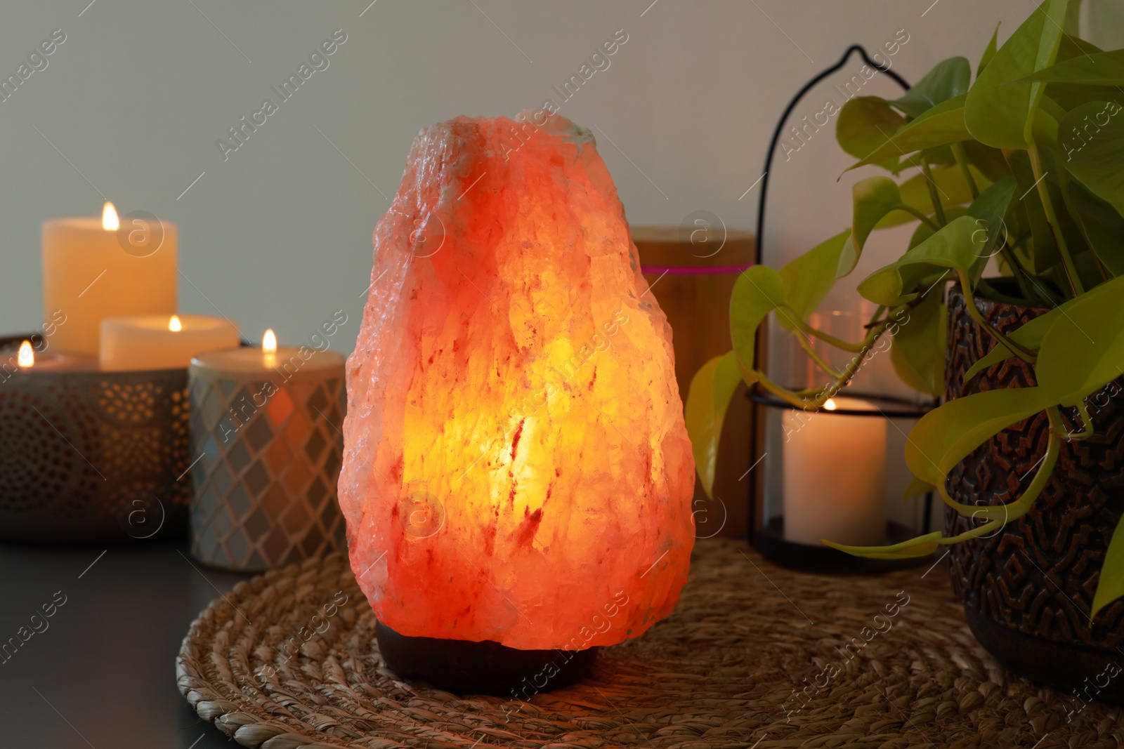 Photo of Himalayan salt lamp, houseplant and candles on table near light wall