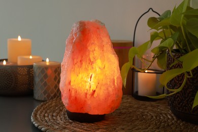 Photo of Himalayan salt lamp, houseplant and candles on table near light wall