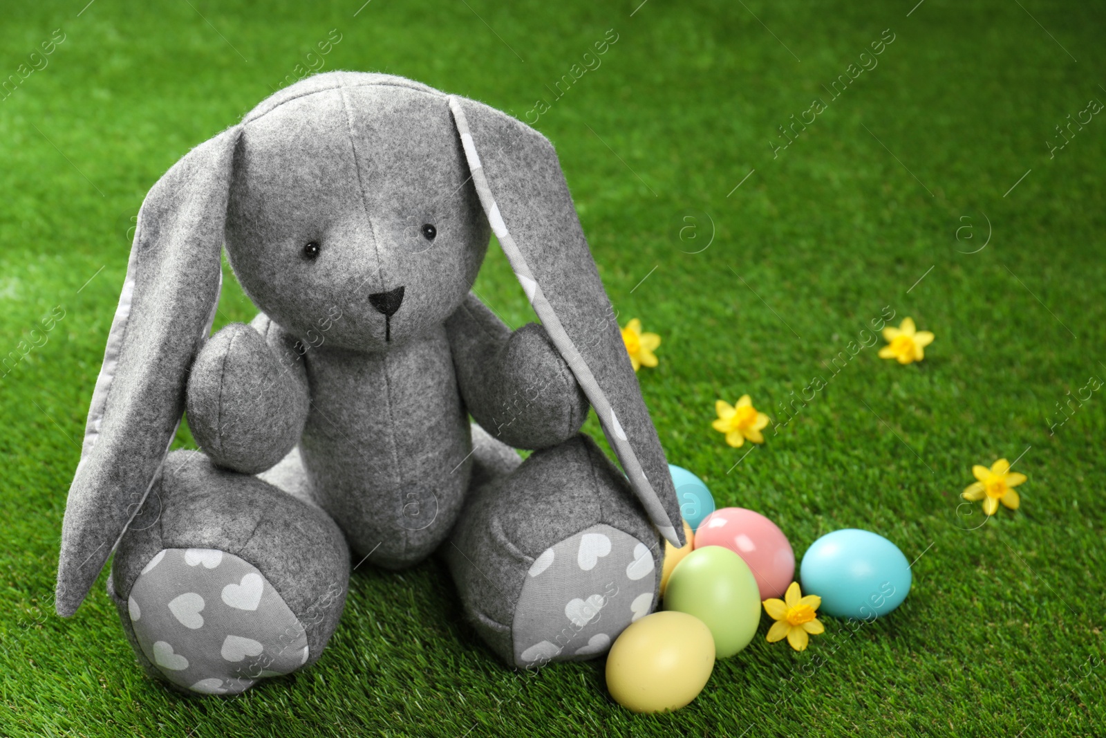 Photo of Cute Easter bunny toy and dyed eggs on green grass, space for text