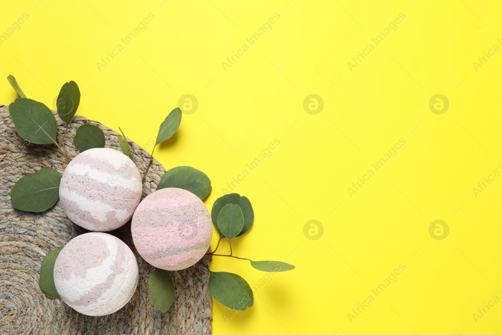 Photo of Bath bombs and eucalyptus leaves on yellow background, flat lay. Space for text