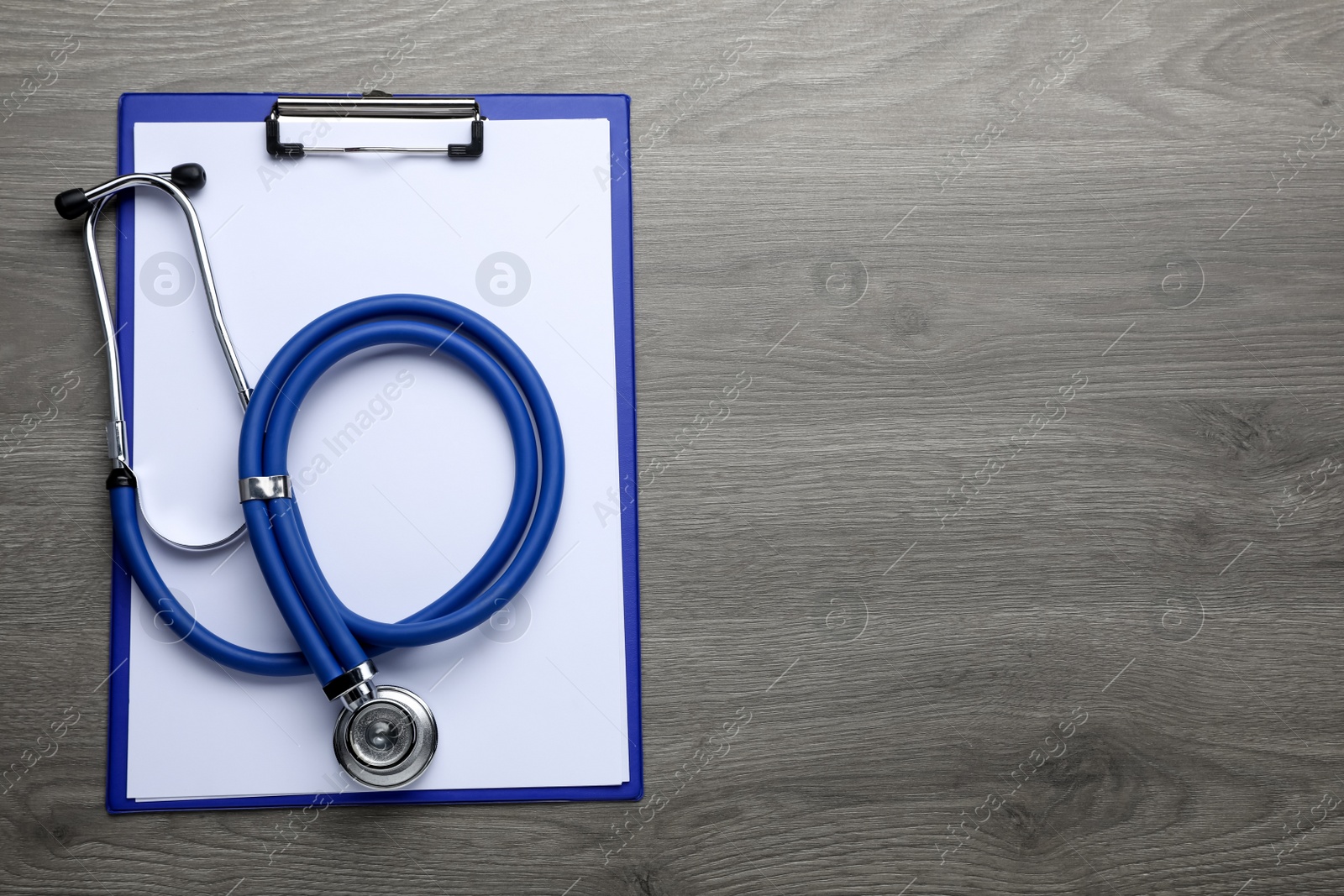 Photo of Clipboard with stethoscope on wooden table, top view. Space for text