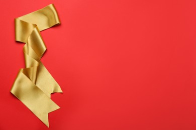 Photo of Beautiful golden ribbon on red background, top view. Space for text
