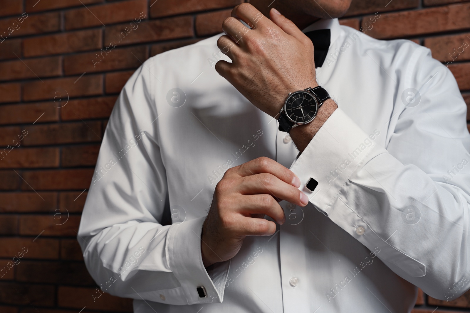 Photo of Stylish man putting on cufflink near brick wall, closeup