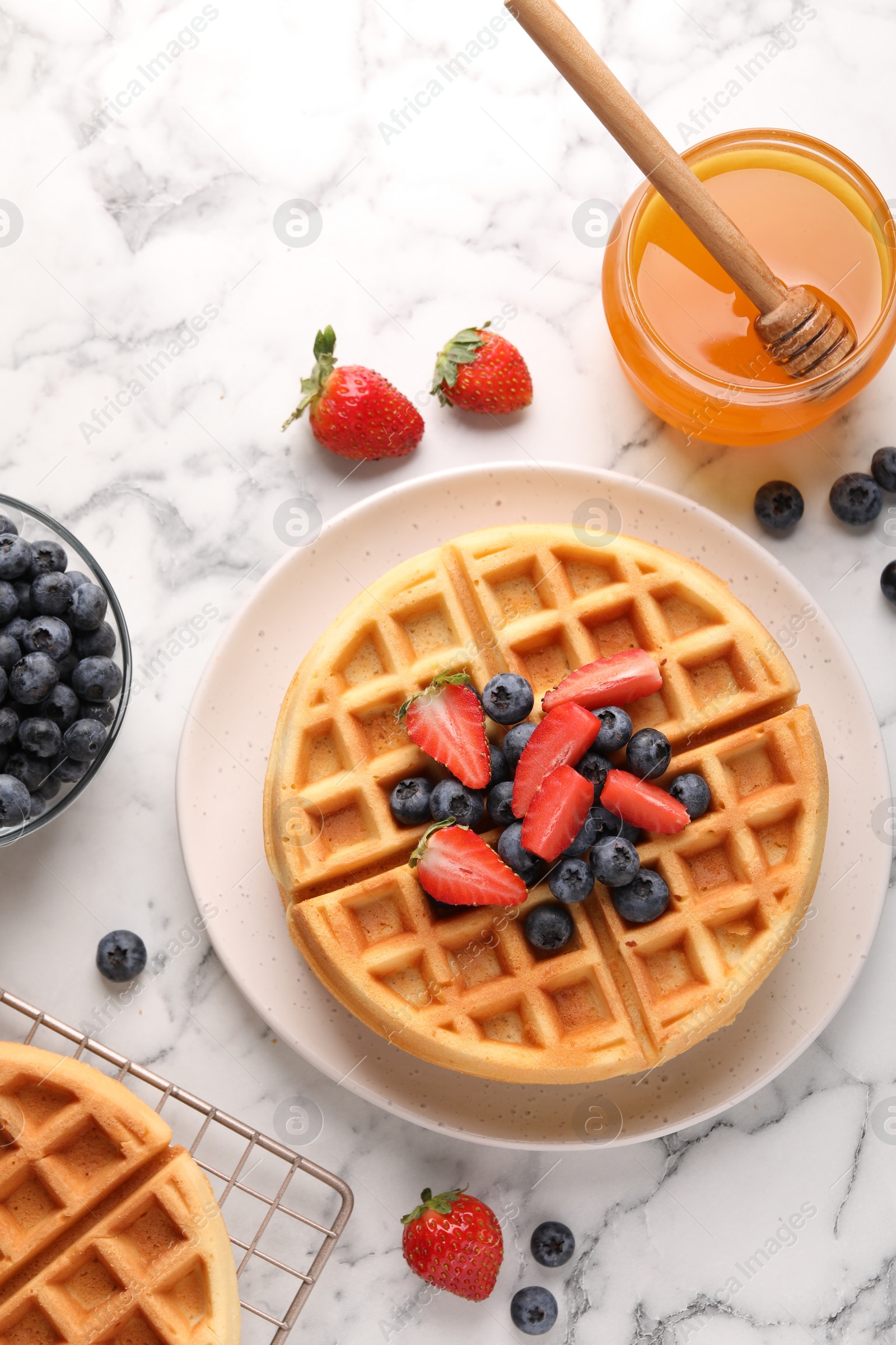 Photo of Tasty Belgian waffles with fresh berries and honey on white marble table, flat lay