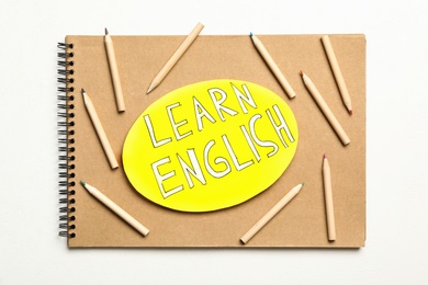 Photo of Notepad with phrase Learn English and pencils on white background, top view