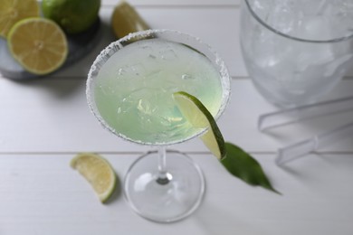 Delicious Margarita cocktail in glass and limes on white wooden table, above view