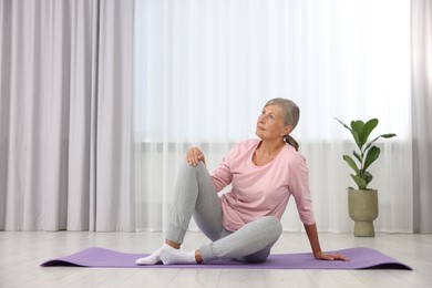 Senior woman sitting on mat at home. Yoga practice