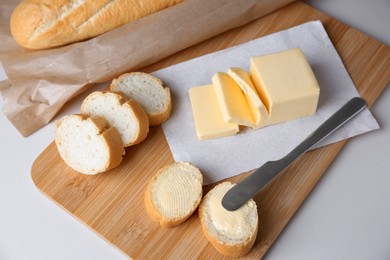 Photo of Tasty cut baguette with fresh butter on white table