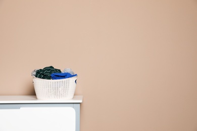 Photo of Plastic laundry basket with dirty clothes on chest of drawers near color wall. Space for text