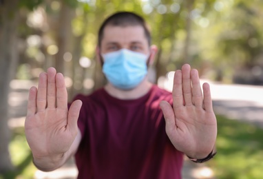 Photo of Man in protective face mask showing stop gesture outdoors, focus on hands. Prevent spreading of coronavirus