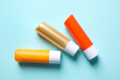 Photo of Hygienic lipsticks on turquoise background, flat lay