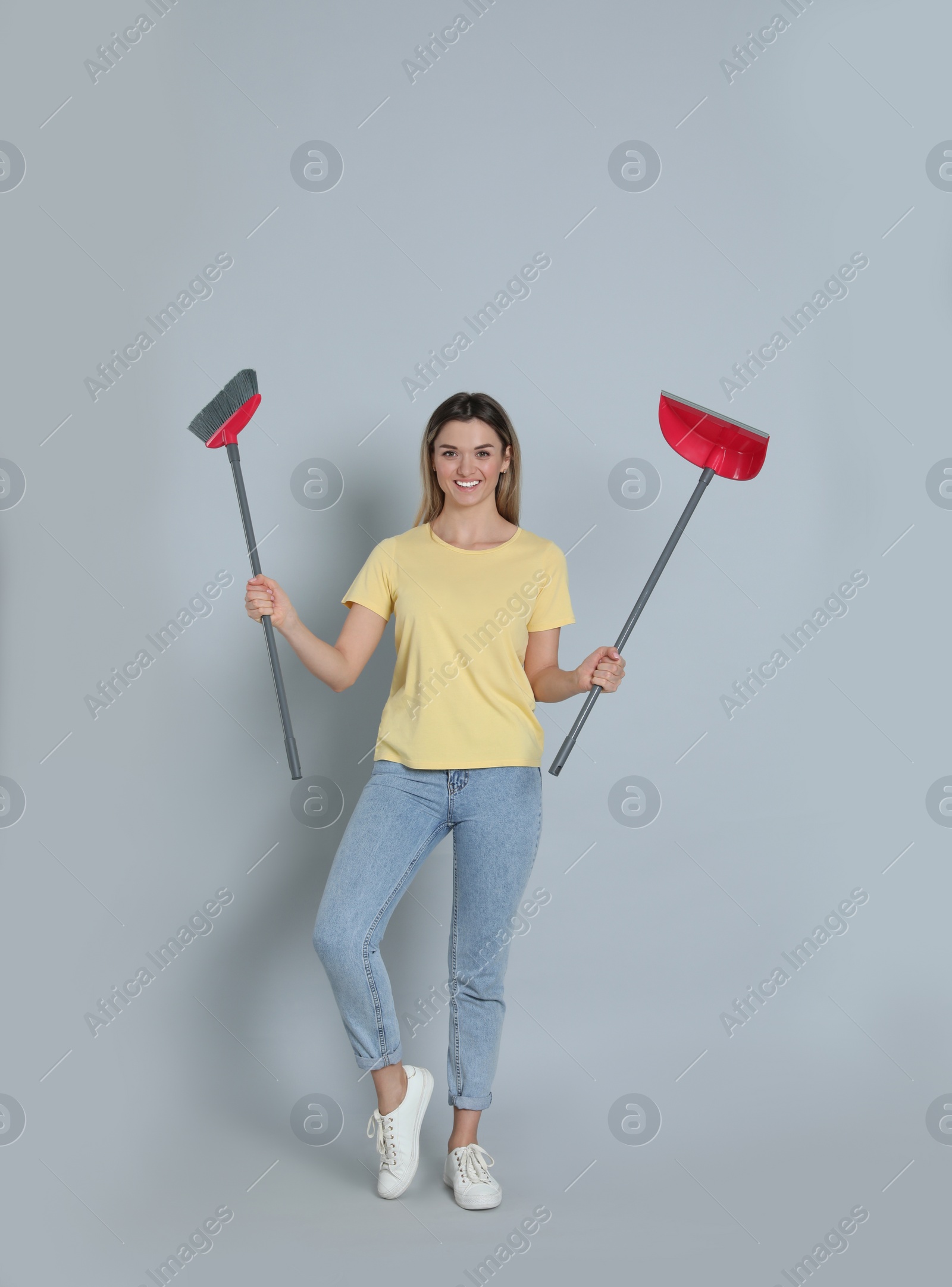 Photo of Young woman with broom and dustpan on grey background