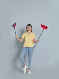 Young woman with broom and dustpan on grey background