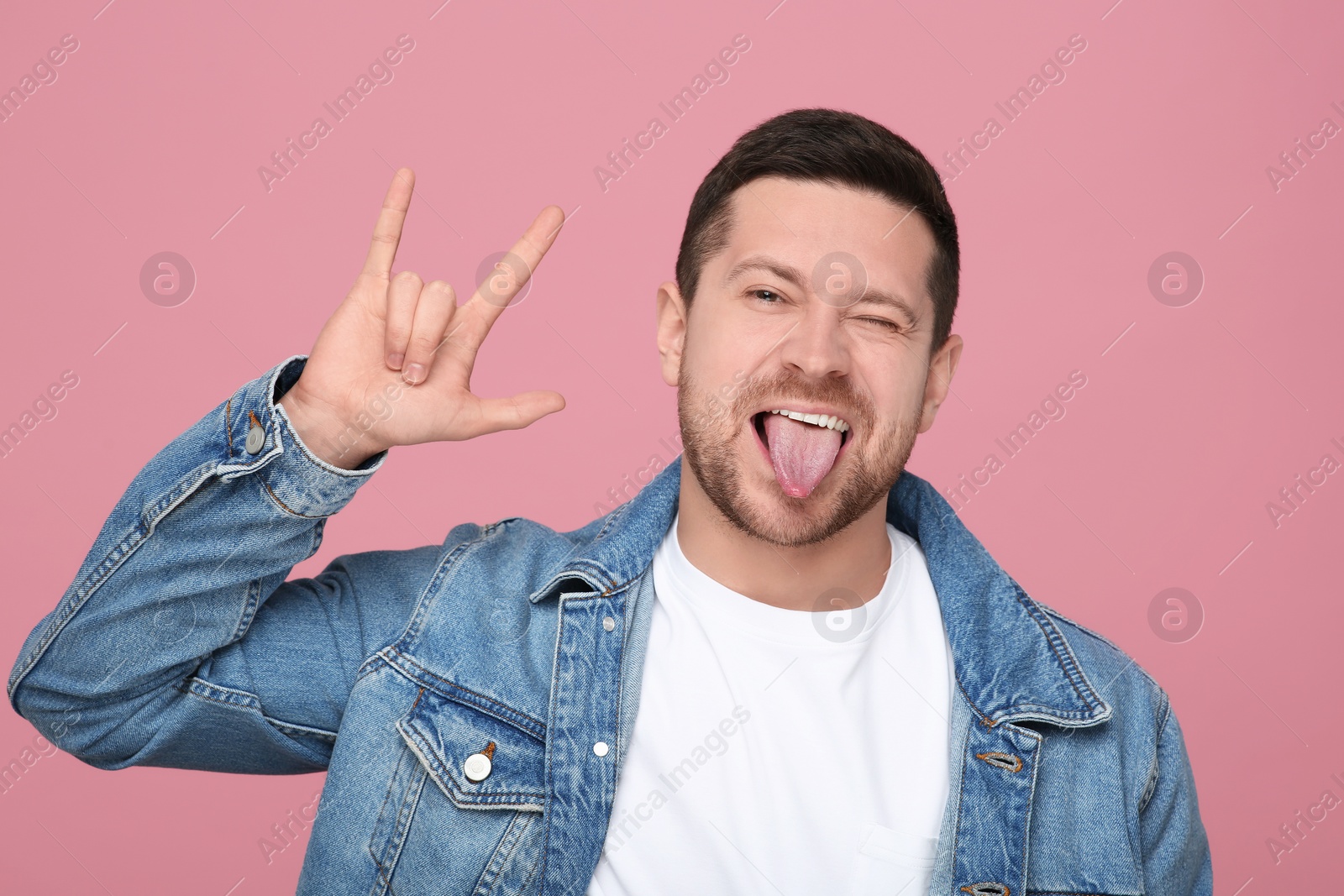 Photo of Happy man showing his tongue and rock gesture on pink background