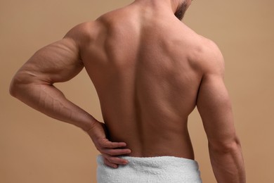 Man suffering from back pain on beige background, closeup