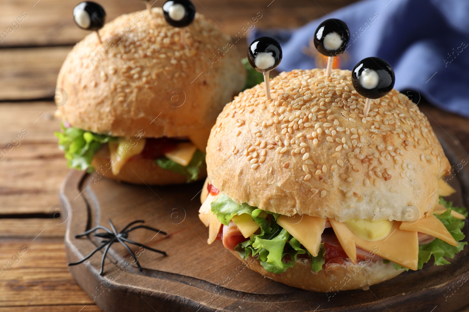 Photo of Cute monster burgers served on wooden board, closeup. Halloween party food