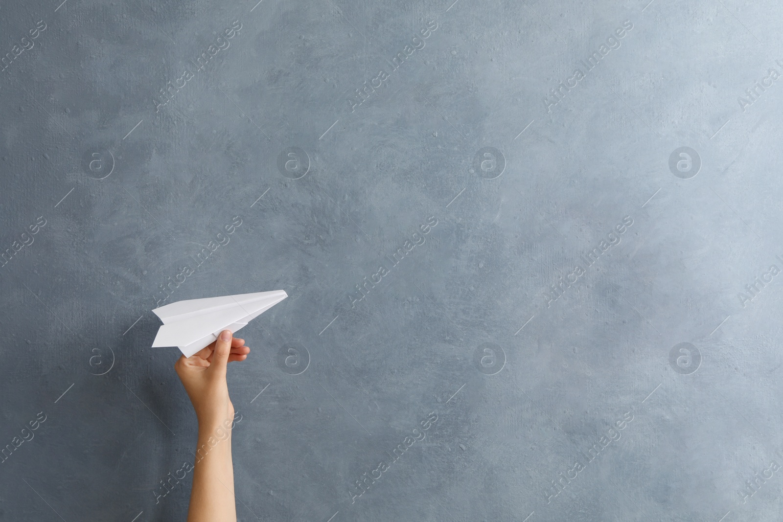 Photo of Woman holding paper plane near grey wall, space for text. Start up concept