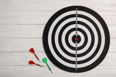 Photo of Dart board with color arrows on white wooden background, top view. Space for text