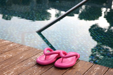 Photo of Pink flip flops on wooden deck near outdoor swimming pool