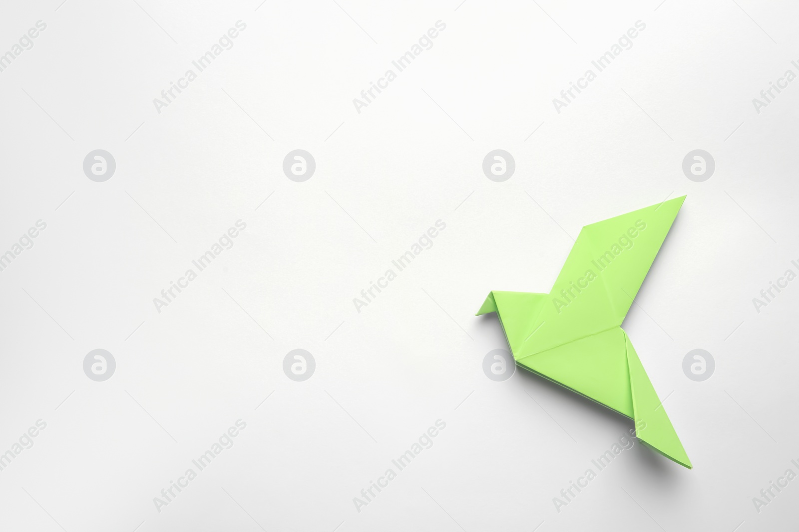 Photo of Beautiful light green origami bird on white background, top view. Space for text