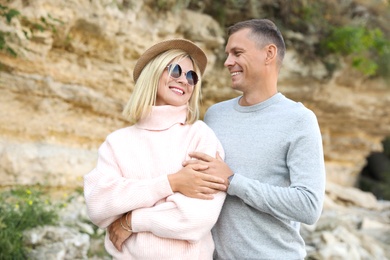 Happy couple in stylish sweaters near old cliff