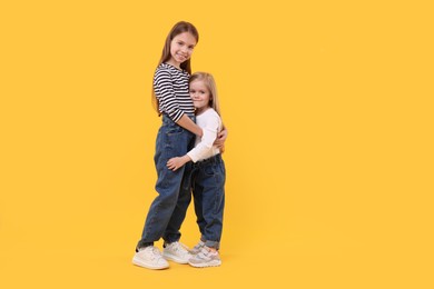 Full length portrait of cute little sisters on orange background, space for text